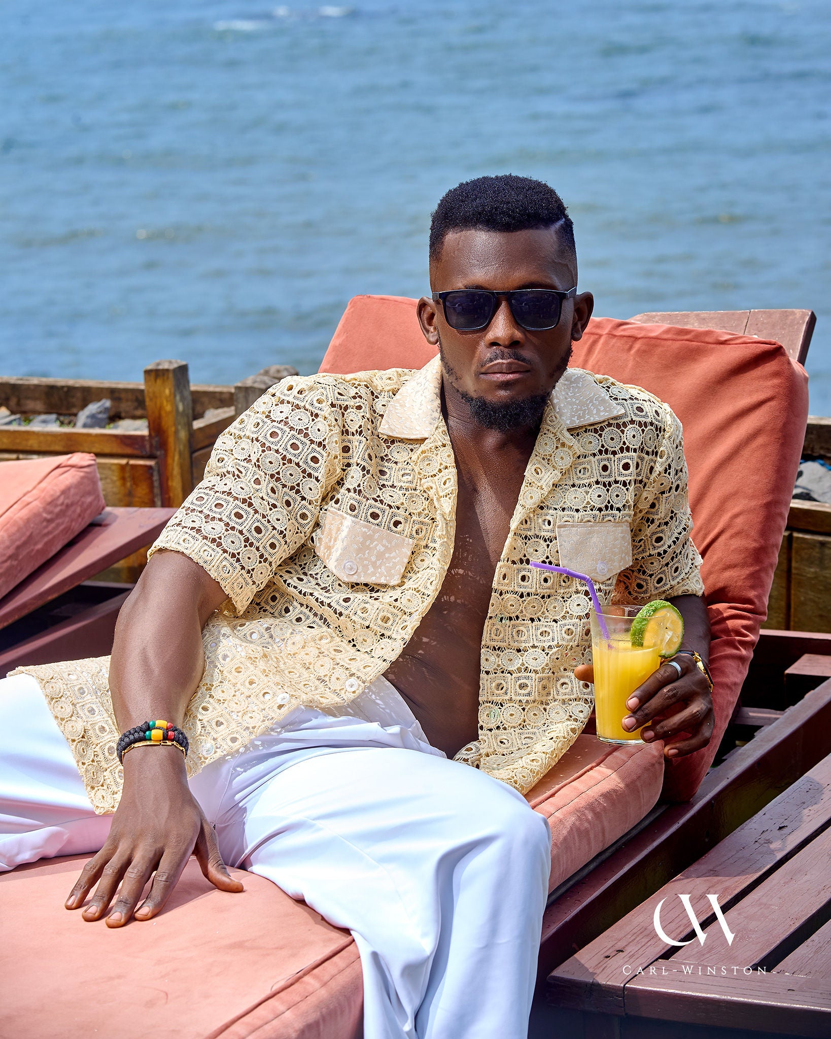 Man relaxing by the ocean wearing a beige cotton lace shirt and white pants by Carl-Winston.