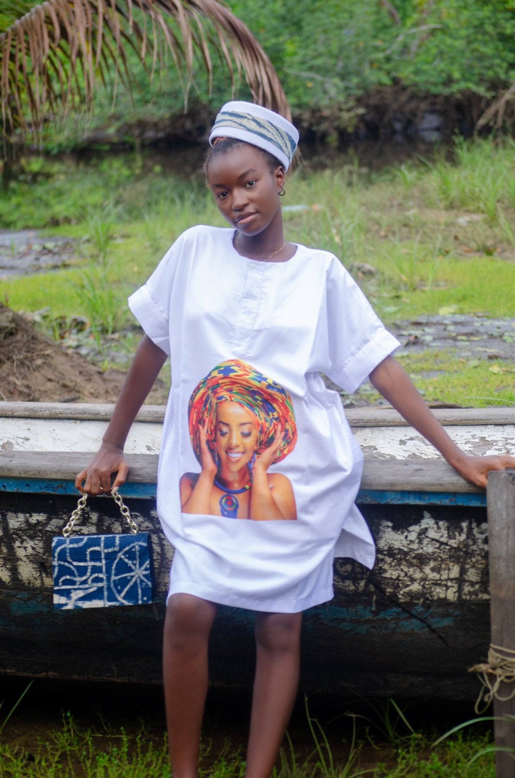 African woman wearing a blue dress vibrant graphic print of a smiling woman in a traditional head wrap, seated with a matching blue patterned handbag  African-inspired fashion with cultural and artistic flair Carl-Winston