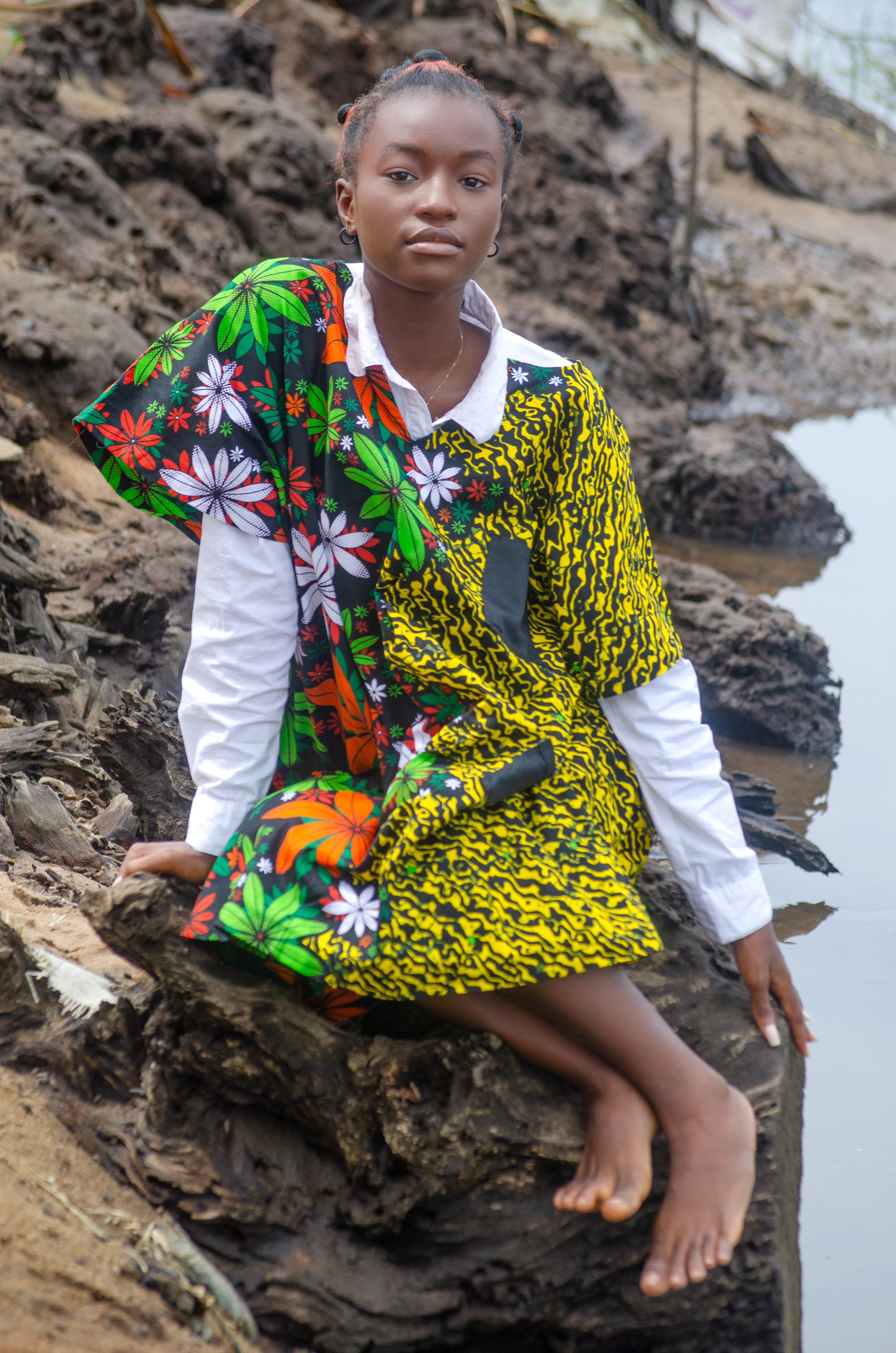 African woman wearing a vibrant, mixed-pattern Carl-Winston dress featuring bold floral and abstract designs combines traditional African prints with contemporary flair