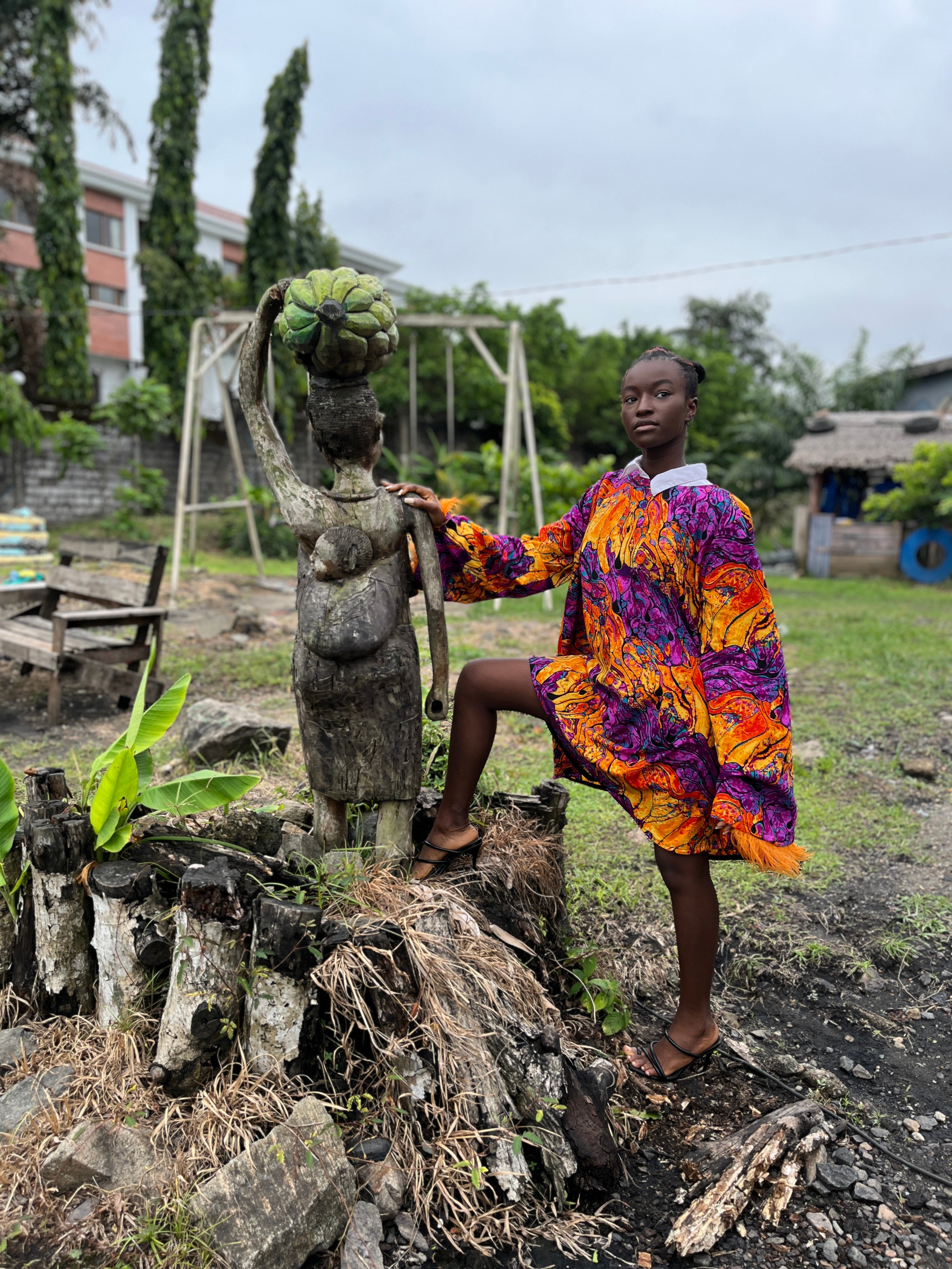 African woman wearing a colorful Carl-Winston oversized dress with bold orange, purple, and yellow abstract patterns