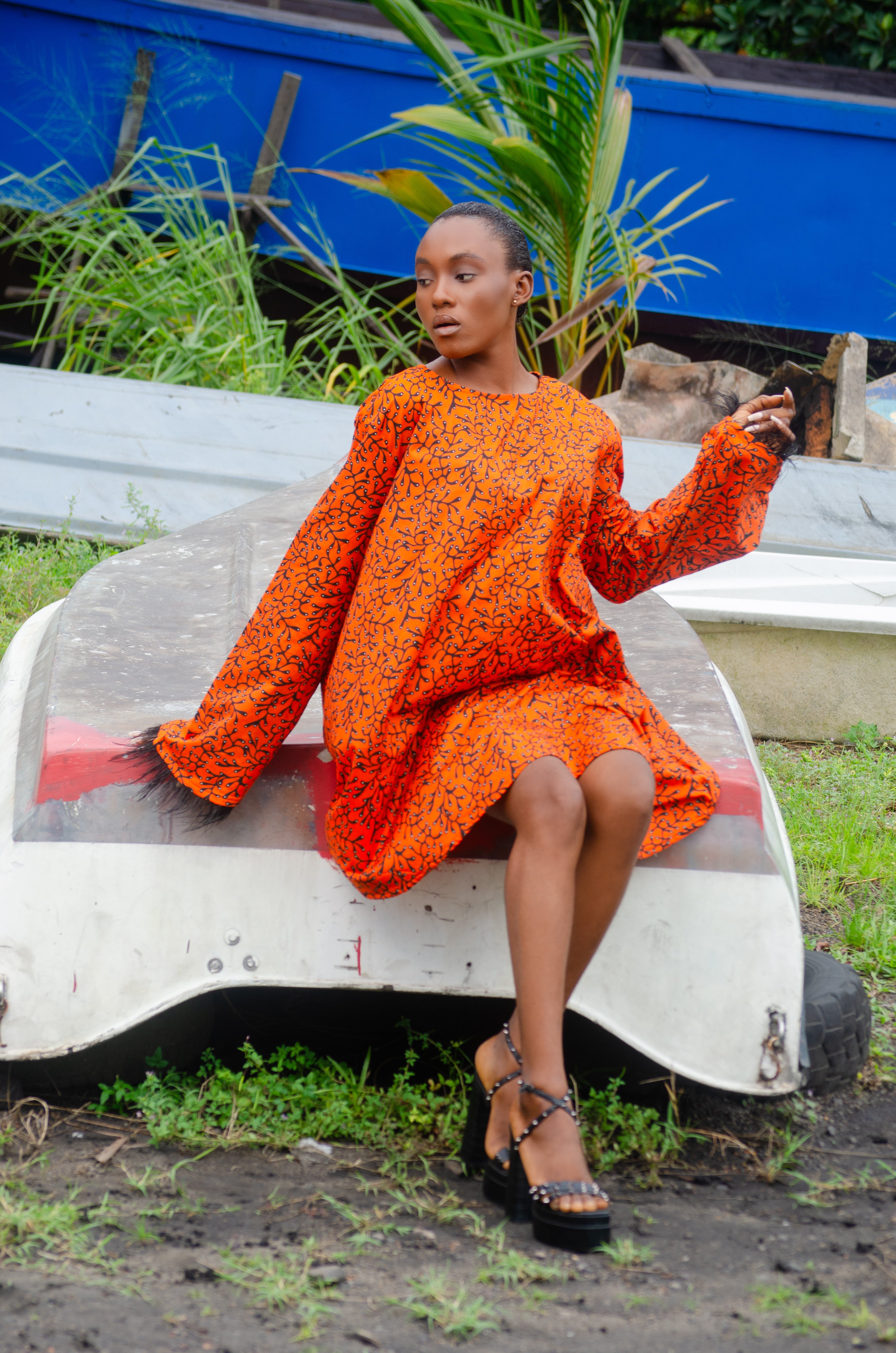 African woman in a bold Carl-Winston oversized dress featuring vibrant orange and black abstract patterns with feathered sleeve African attire combines cultural charm with a contemporary flair