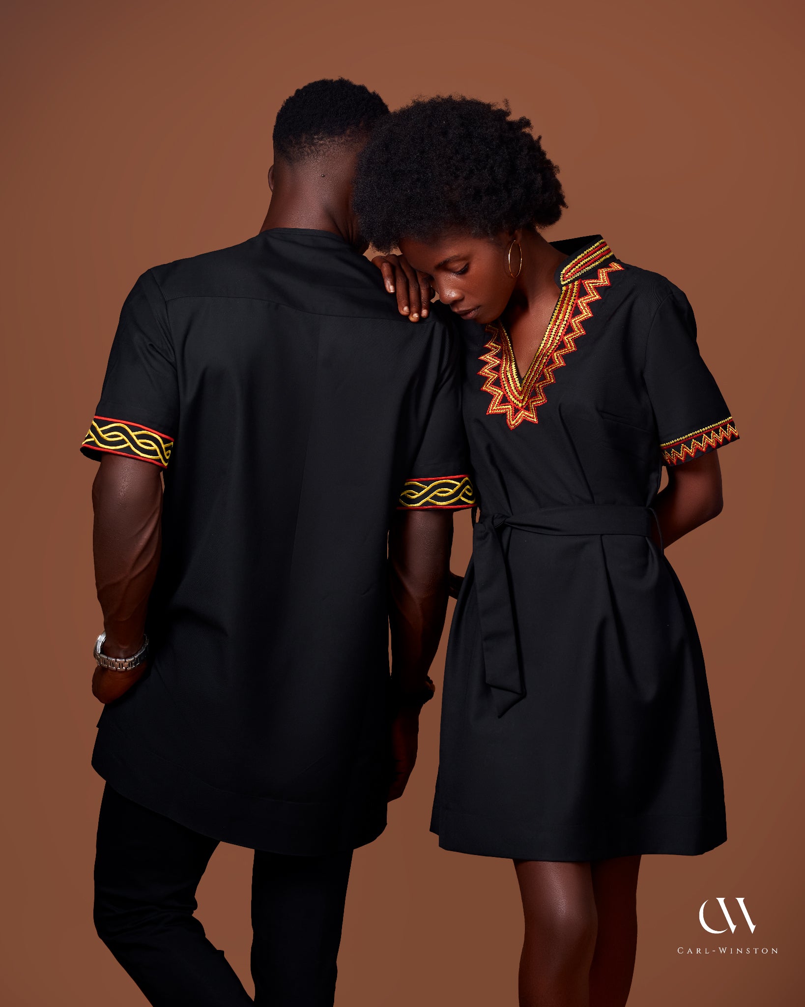 Carl-Winston African-inspired his-and-hers matching outfits. Black tunic and dress set with intricate yellow and red embroidery details, showcasing elegant, coordinated traditional wear for couples.