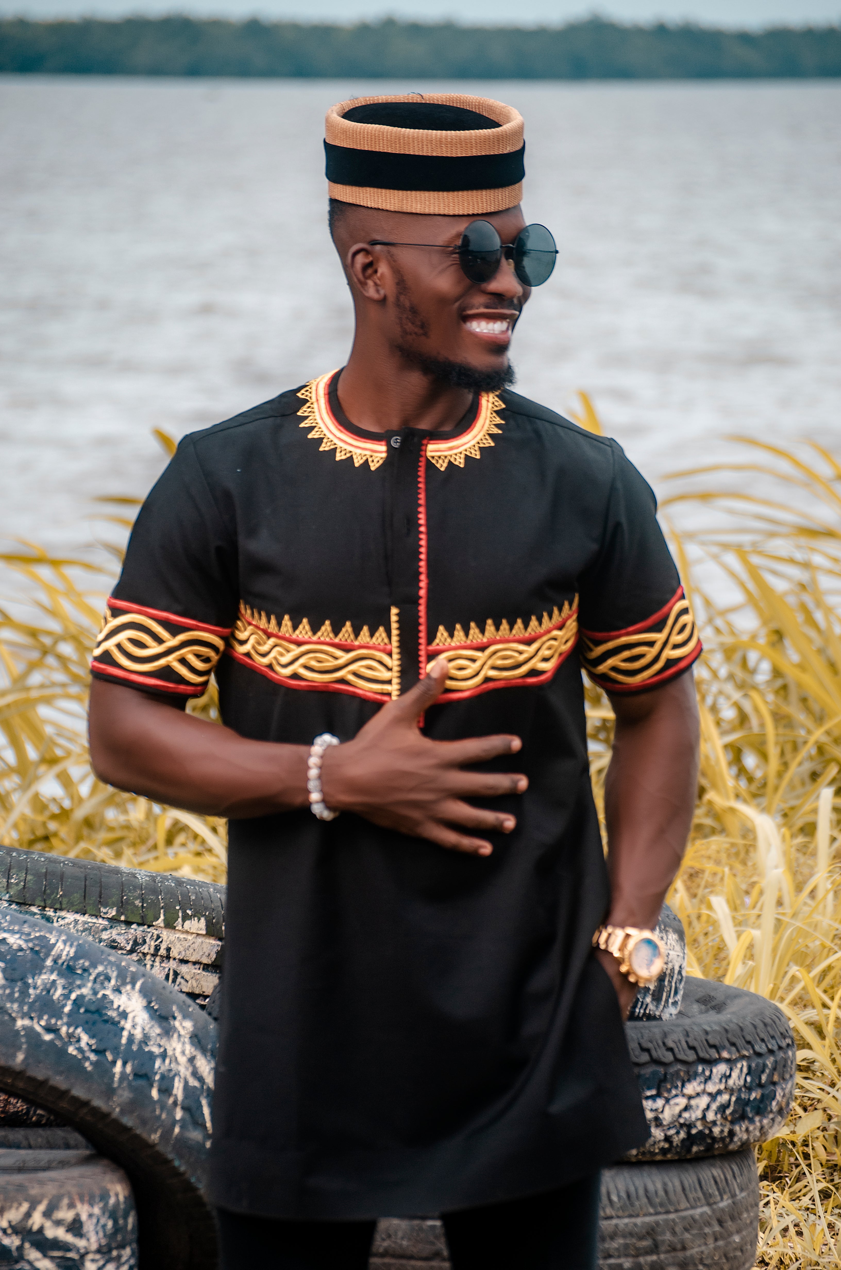 Black man wearing traditional black African tunic with intricate yellow and red embroidery, paired with a matching woven hat Afrocentric fashion 