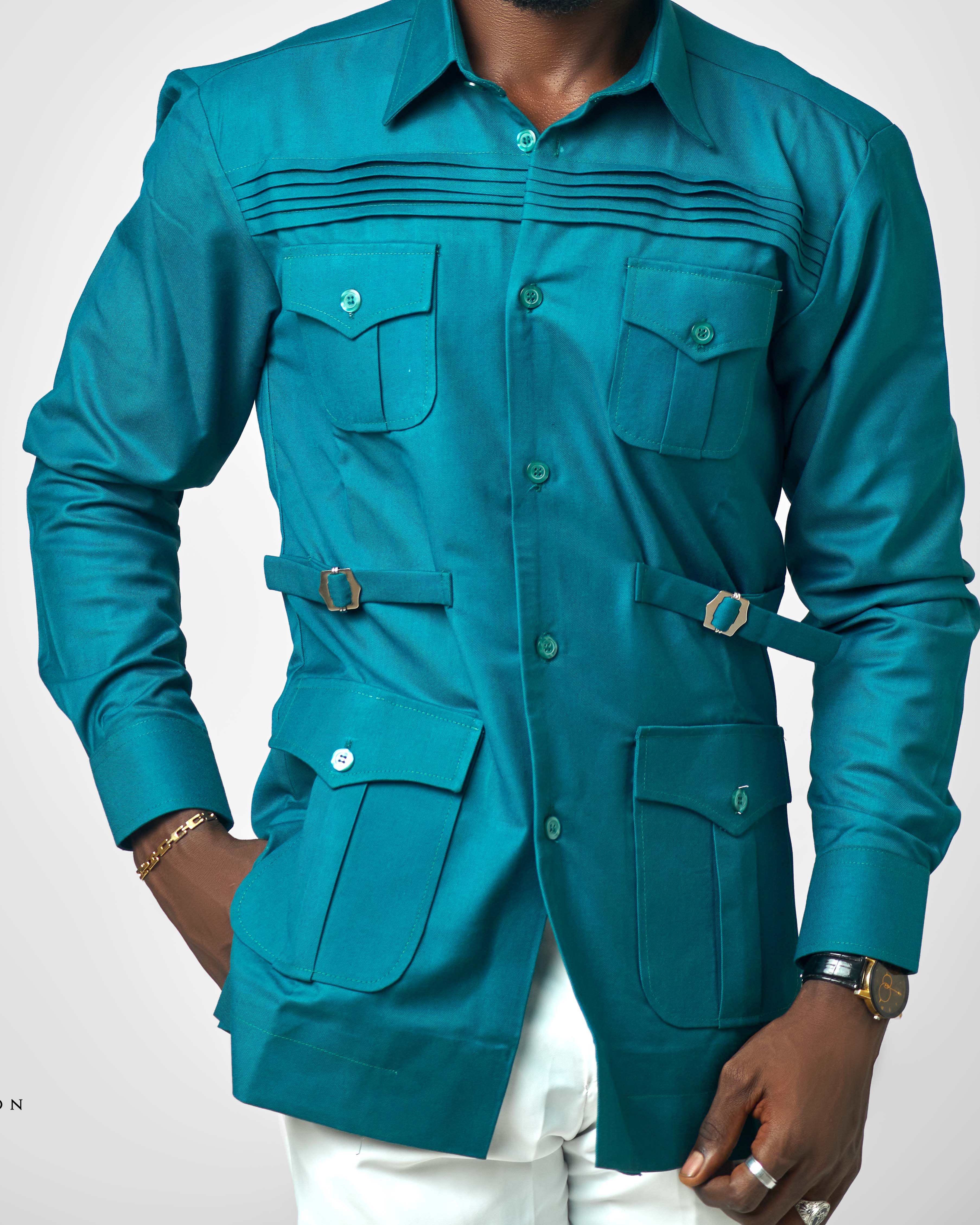 A modern teal men's utility shirt with front pockets, side belt accents, and pleated detailing across the chest, styled by Carl-Winston.
