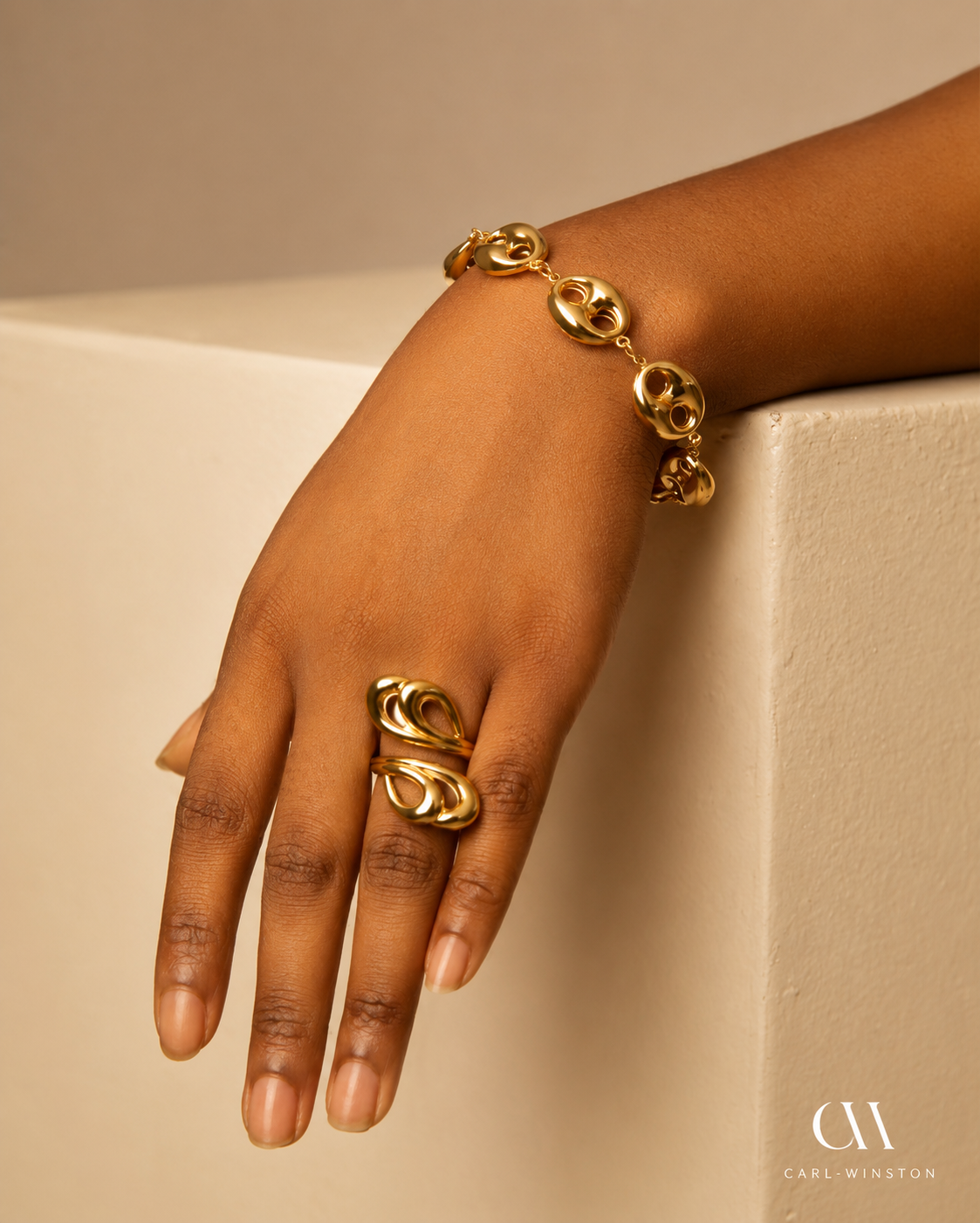 Hand wearing a gold bracelet and ring on a beige background