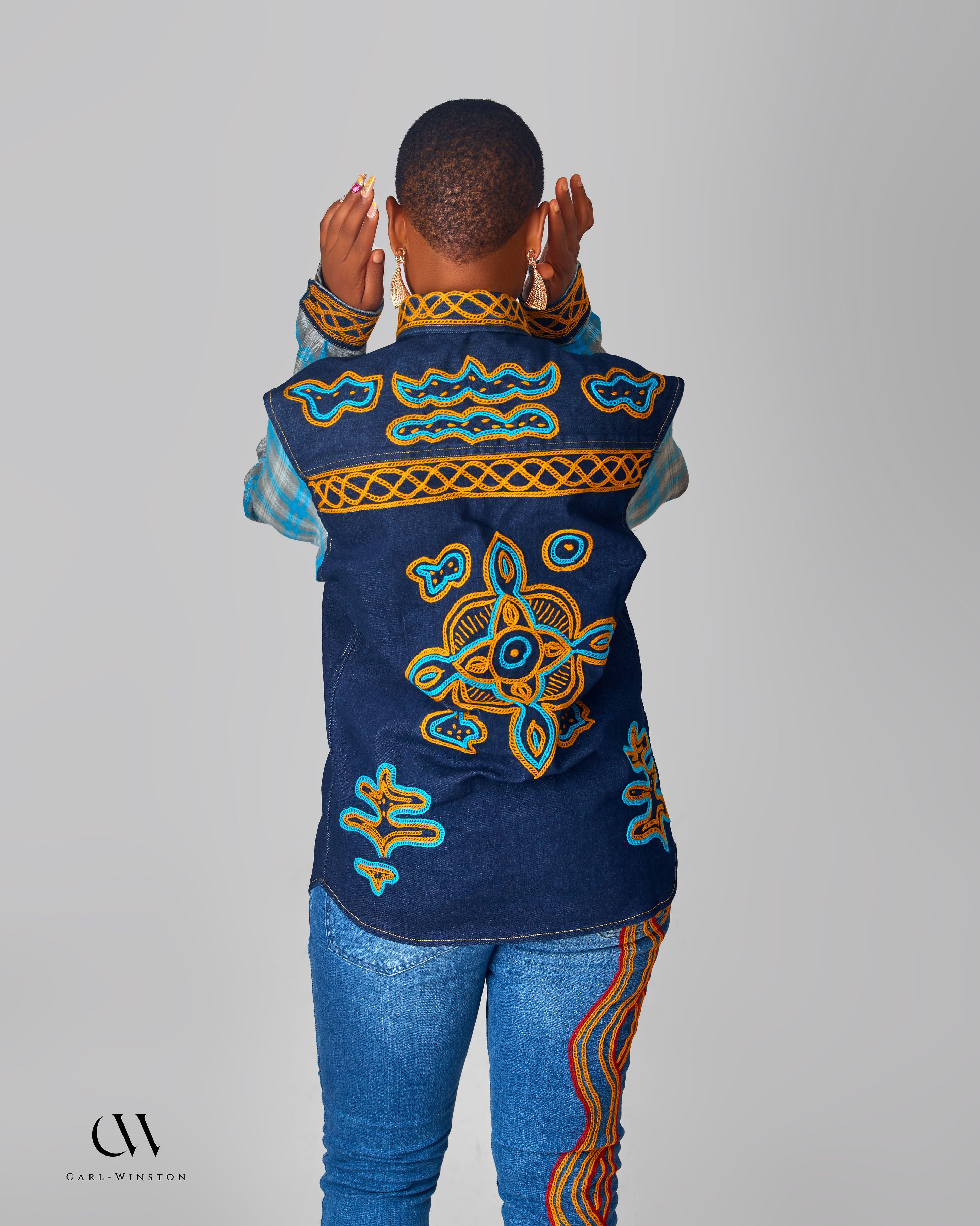 Person wearing a blue embroidered vest with intricate patterns on a gray background