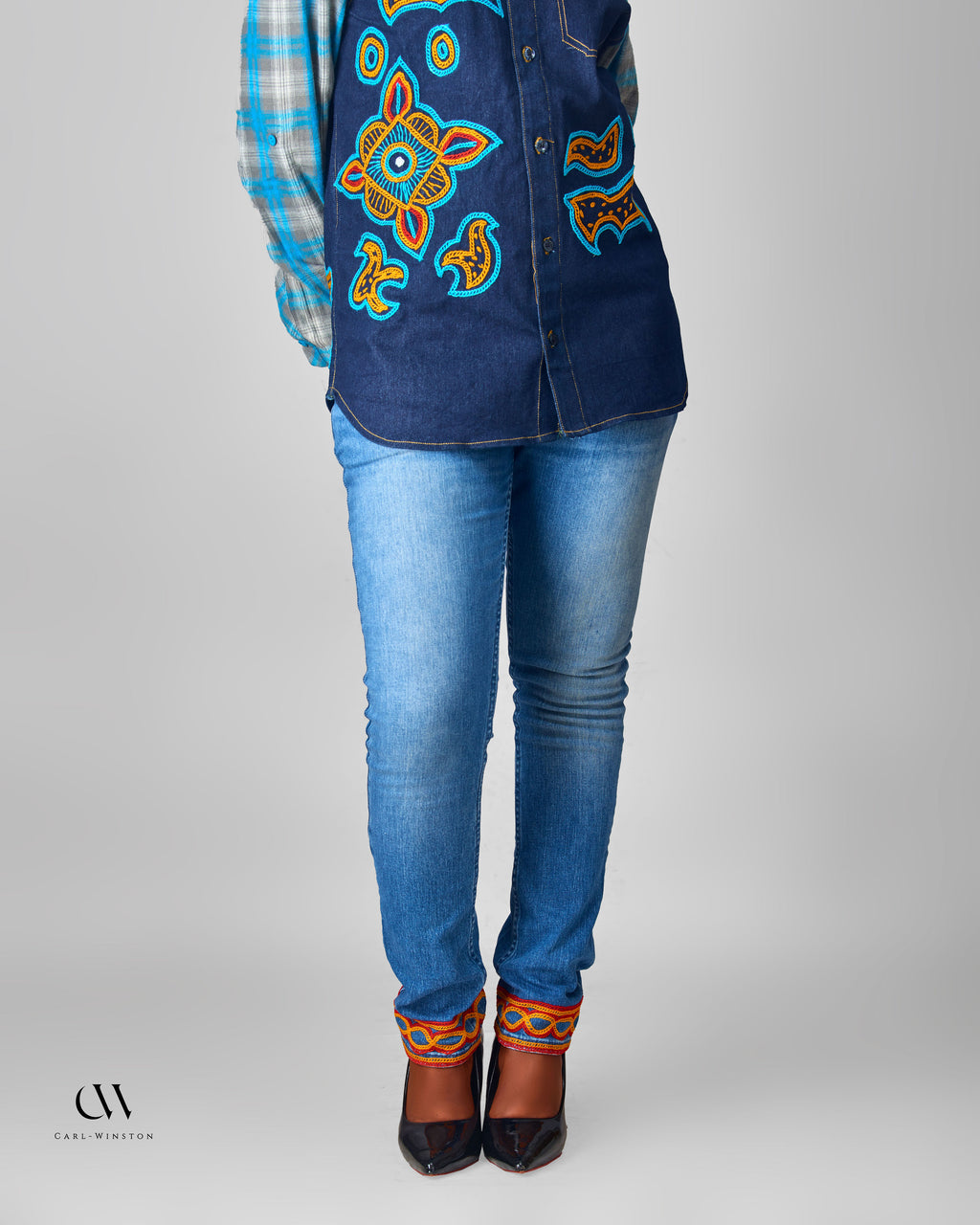 Person wearing a blue embroidered top, jeans, and patterned shoes on a gray background