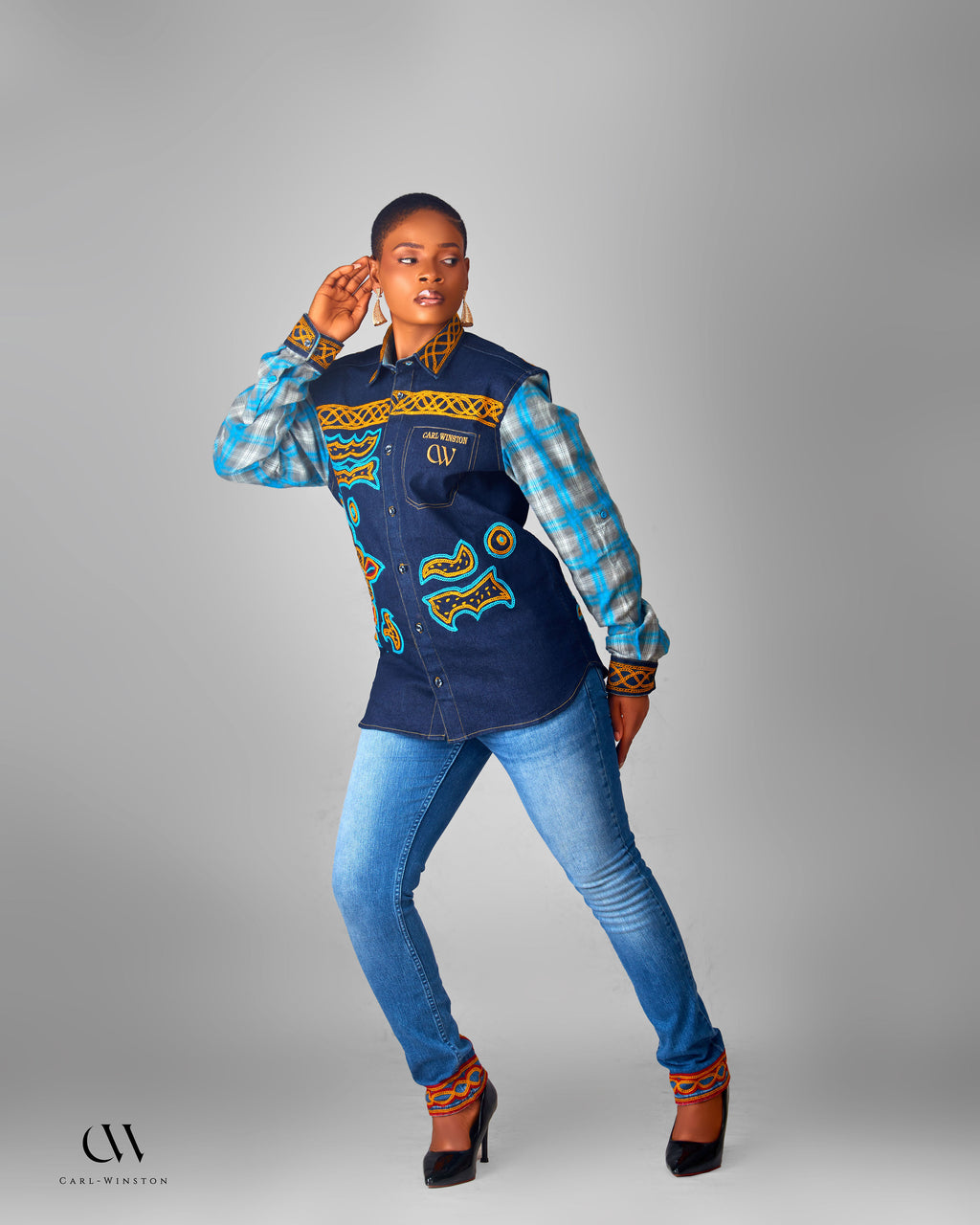 Woman wearing a colorful jacket with patterned design and blue jeans on a gray background