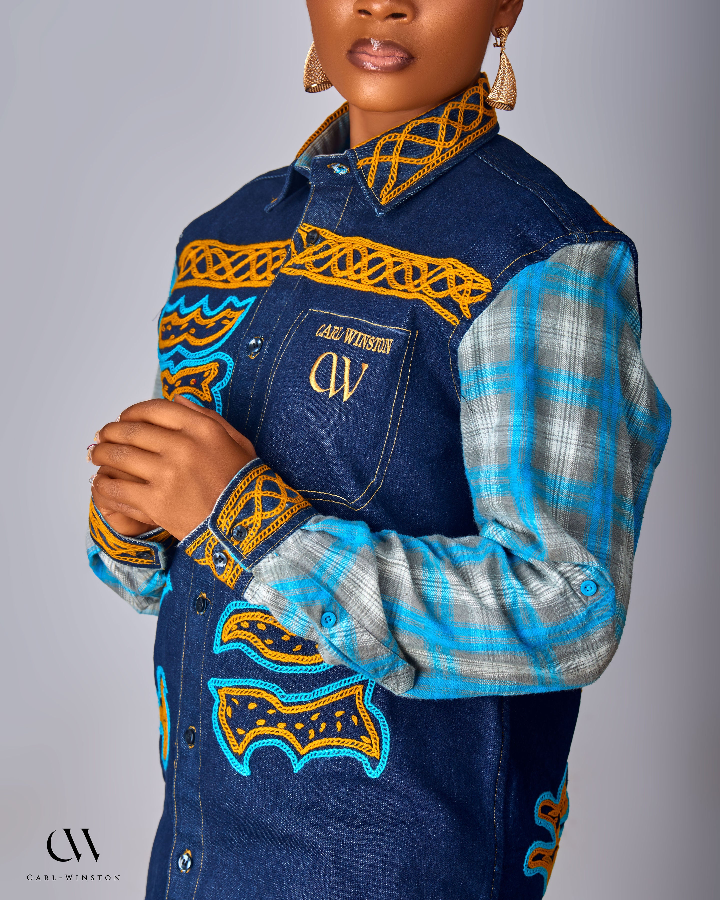 Person wearing a blue denim jacket with intricate yellow and blue patterns on a gray background