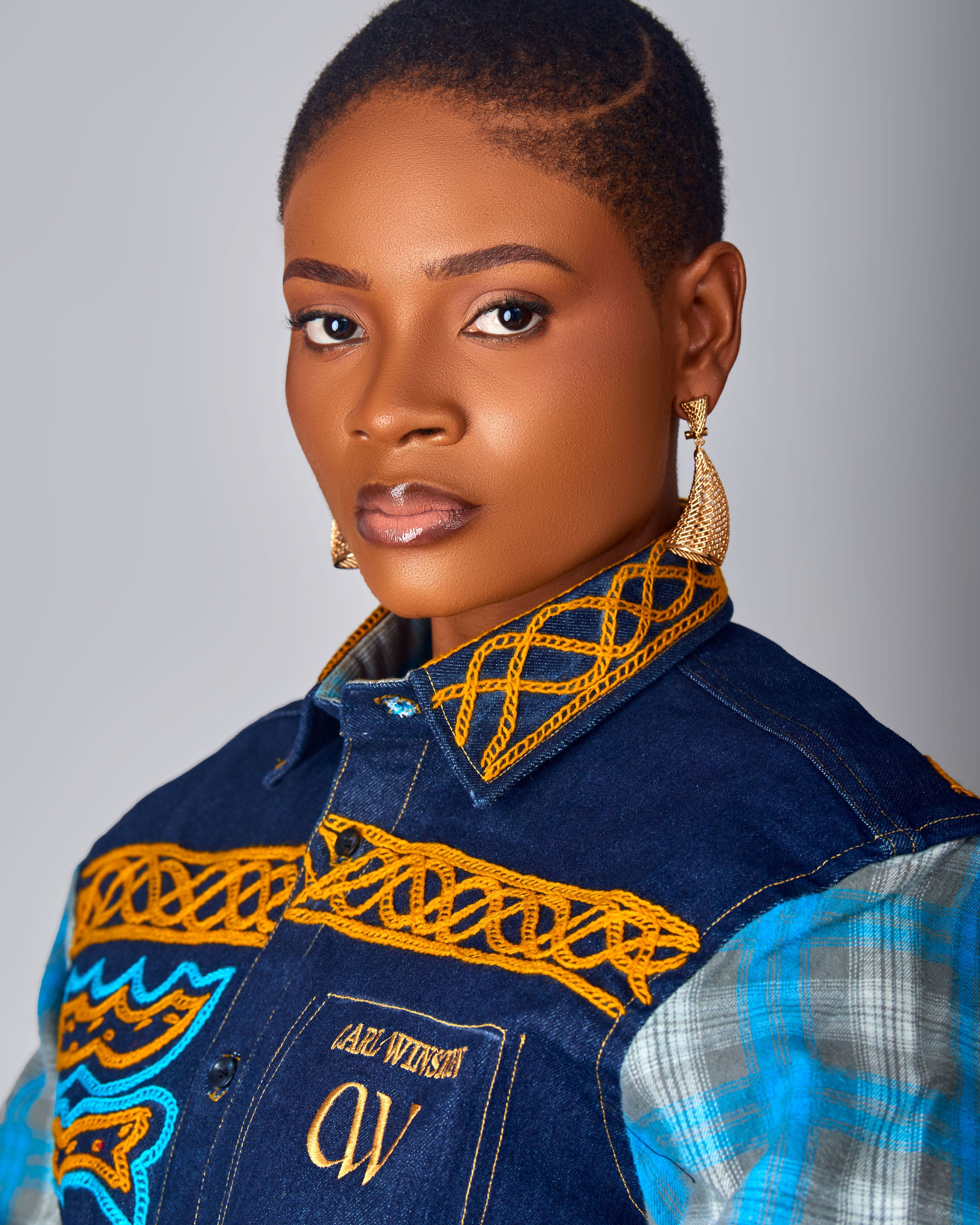 Woman wearing a denim jacket with intricate gold embroidery on a gray background