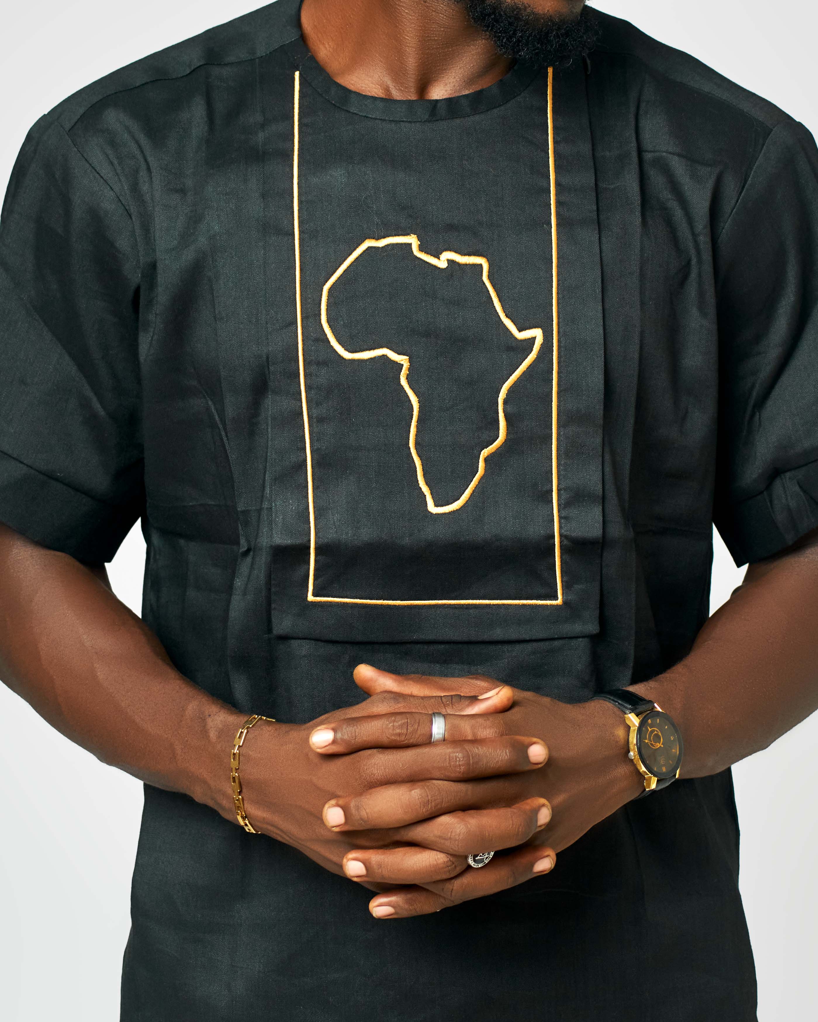 Man wearing a Black short-sleeve linen shirt with an embroidered golden outline of the African continent showcasing bold and cultural fashion.