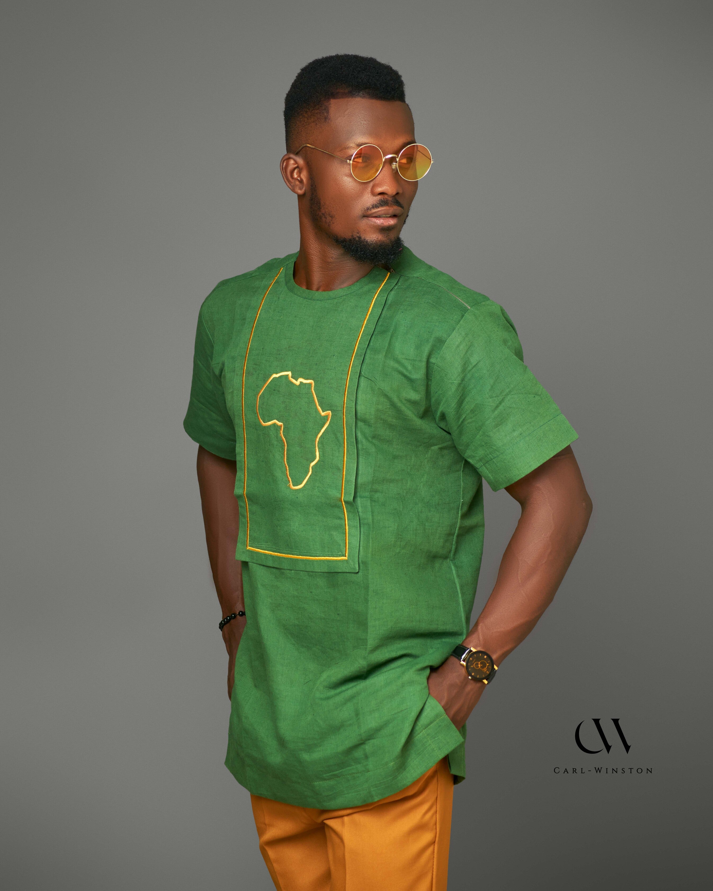 Man wearing a green short-sleeve linen shirt with an embroidered golden outline of the African continent, paired with mustard-yellow pants, showcasing bold and cultural fashion.