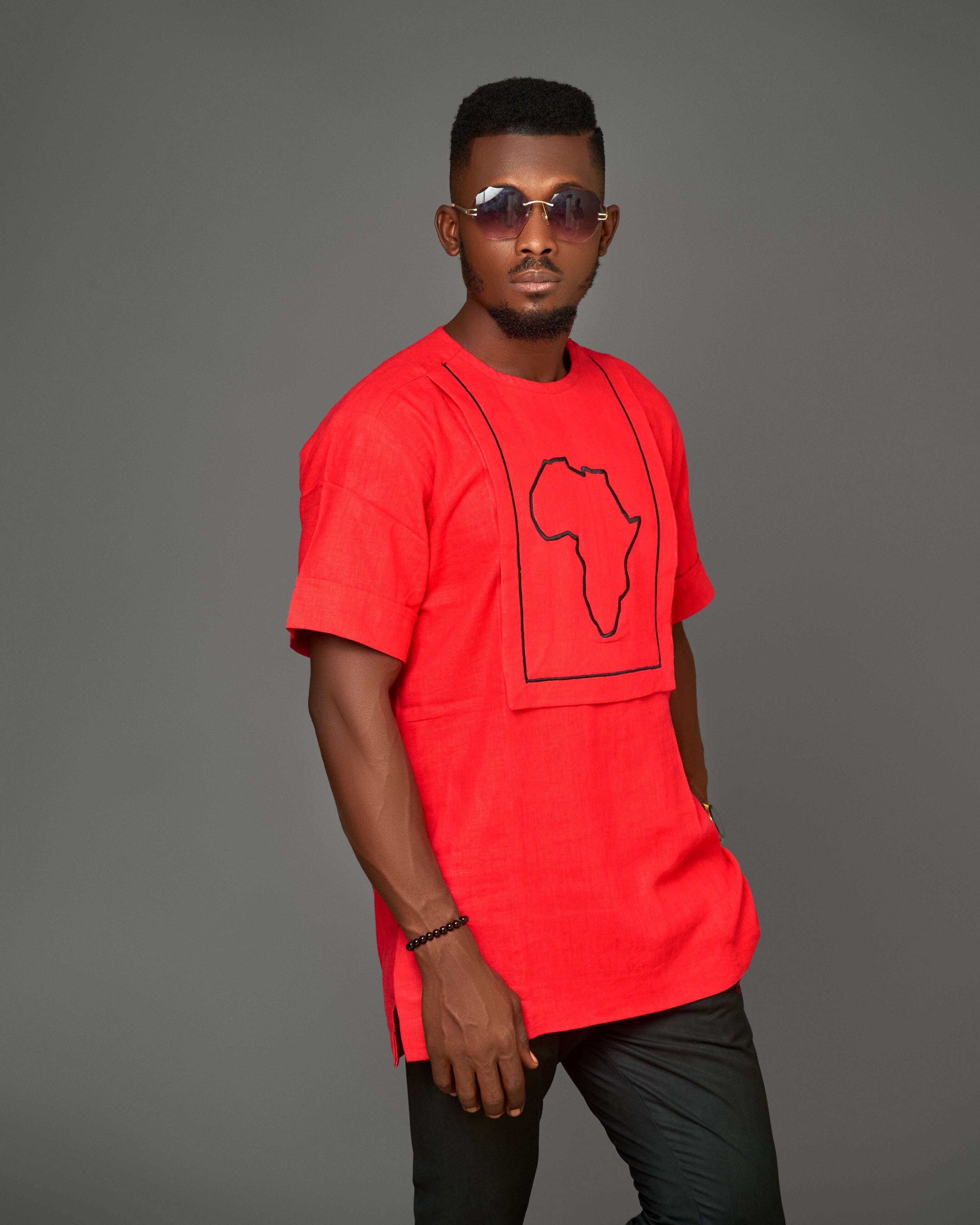 "Man wearing a red short-sleeve linen shirt with an embroidered black outline of the African continent, paired with black pants, showcasing bold and cultural fashion."