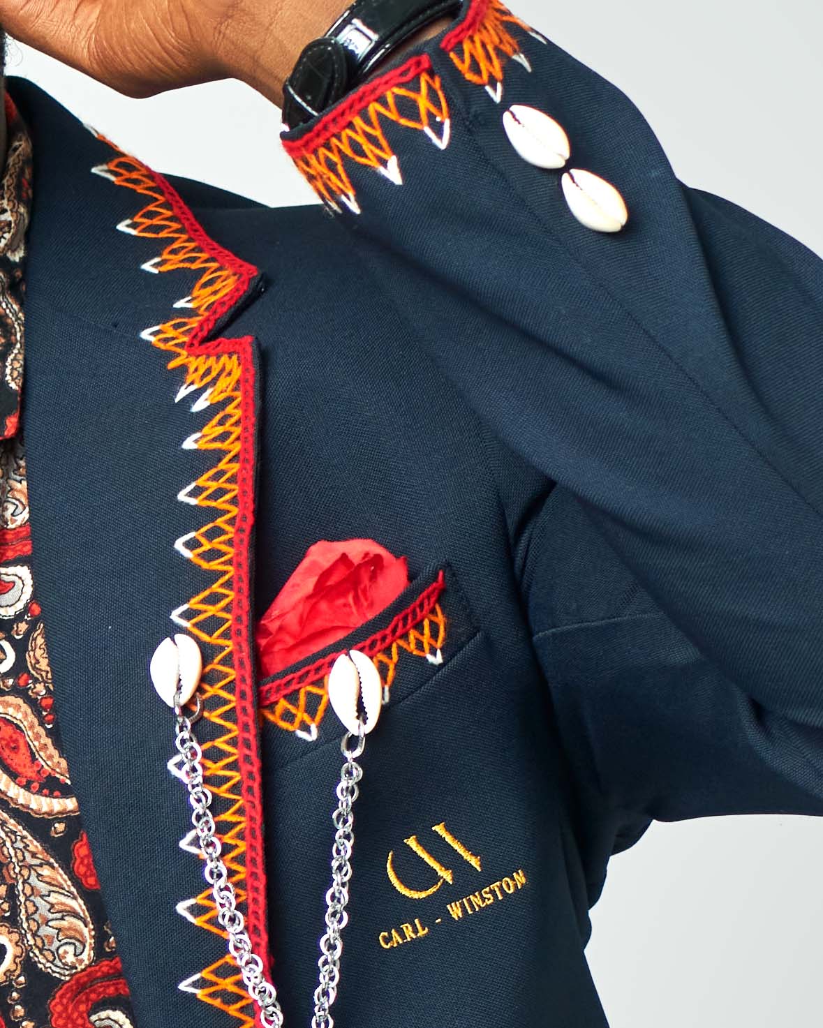 A paisley-print men’s shirt in vibrant colors, styled with a navy blazer and maroon pants for a bold and sophisticated look by Carl-Winston.