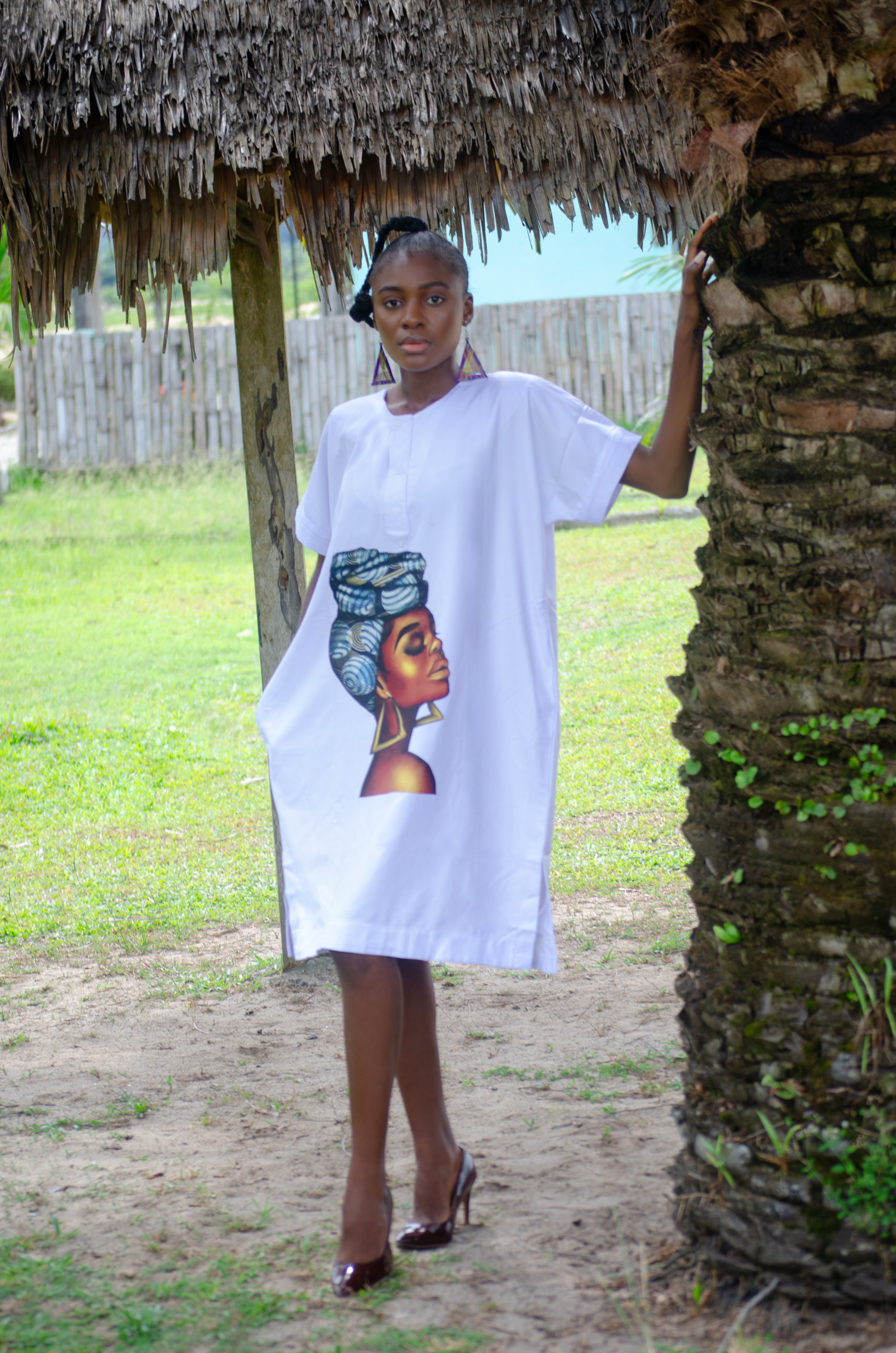 African woman wearing a vibrant white dress with a graphic print of a woman in a head wrap  Perfect for Afrocentric fashion collections highlighting African culture, heritage, and modern elegance Carl-Winston