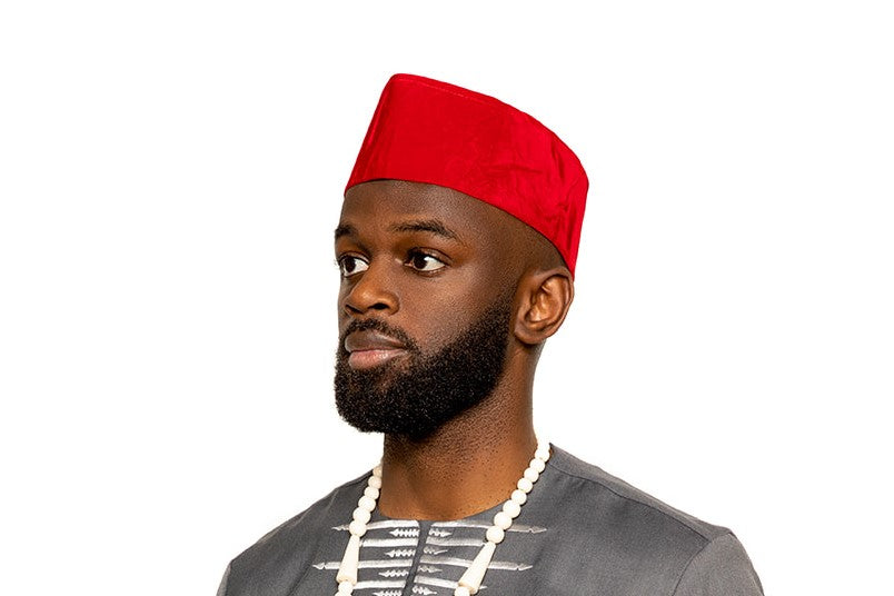 He wears a red traditional hat and a bold beaded necklace featuring claw-like pendants, adding a touch of cultural significance to the ensemble.
