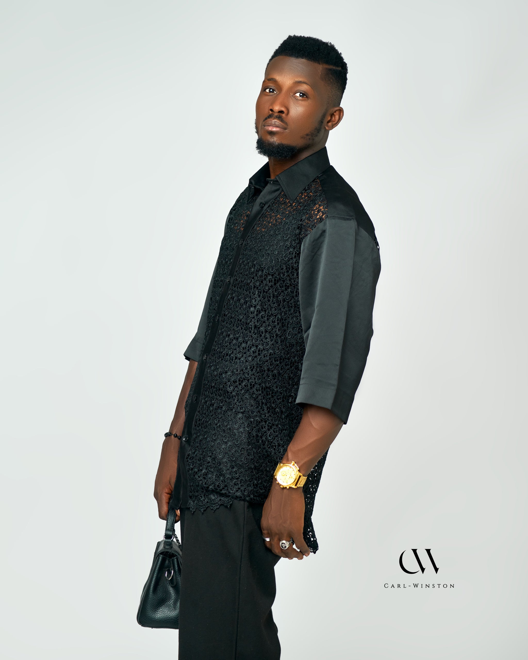 	A stylish model wearing the Noir Elegance Lace Shirt, paired with a sleek black outfit, accessorized with a leather bag and gold watch.