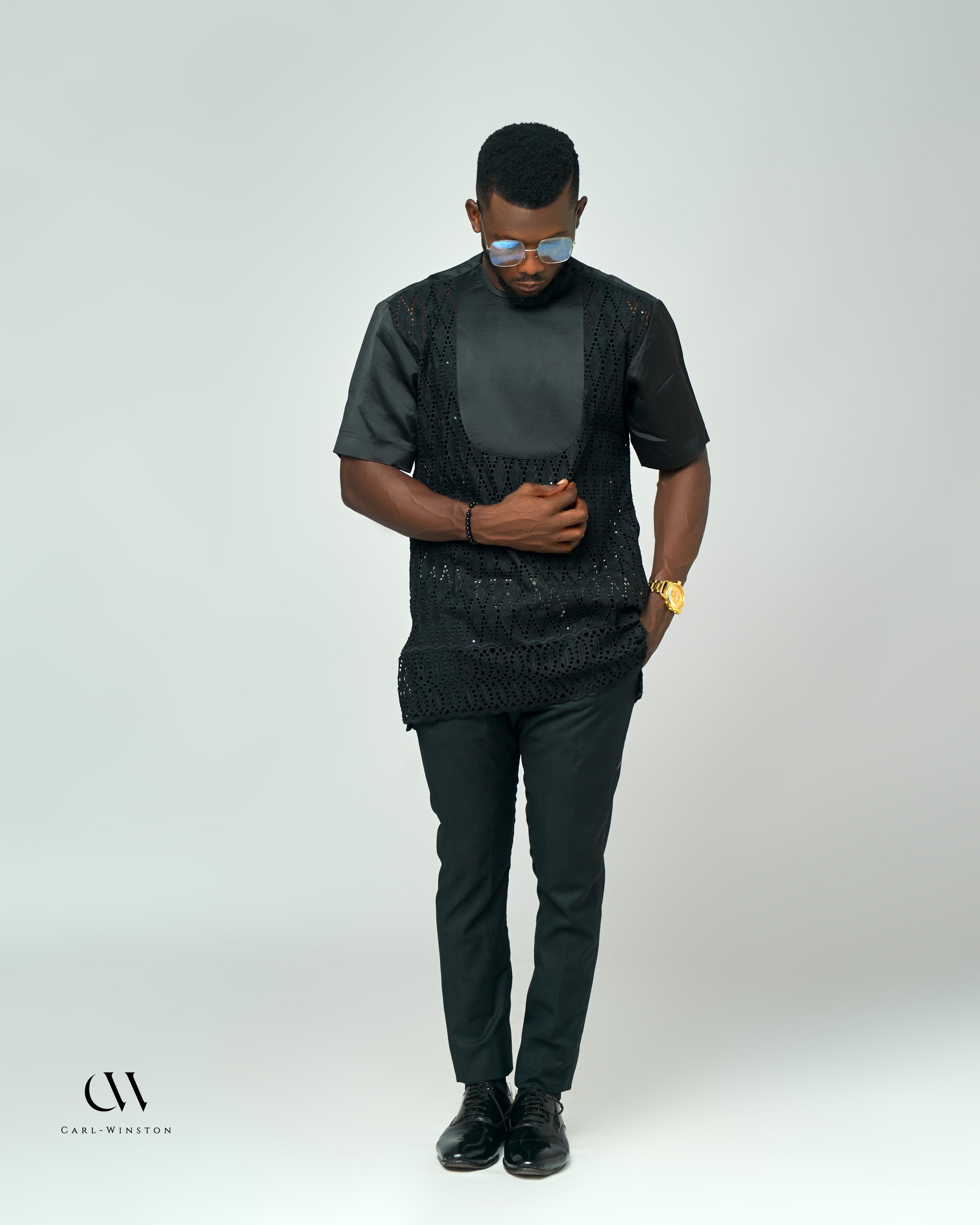 A model wearing the Midnight Lace Elegance Shirt by Carl-Winston, featuring a stunning black lace overlay with satin sleeves, styled with dark trousers and sleek accessories.