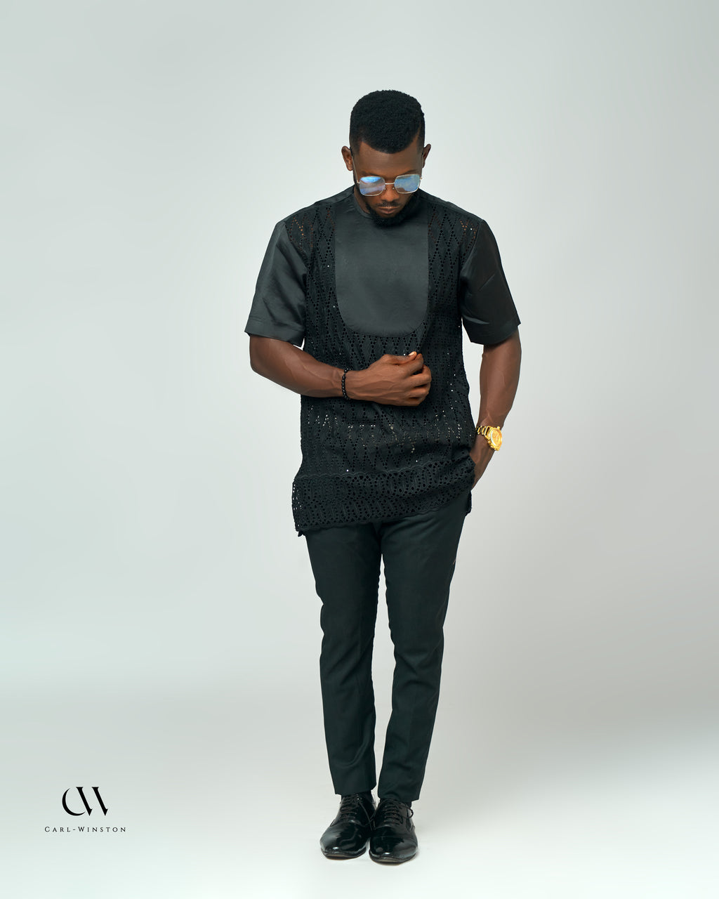 A model wearing the Midnight Lace Elegance Shirt by Carl-Winston, featuring a stunning black lace overlay with satin sleeves, styled with dark trousers and sleek accessories.