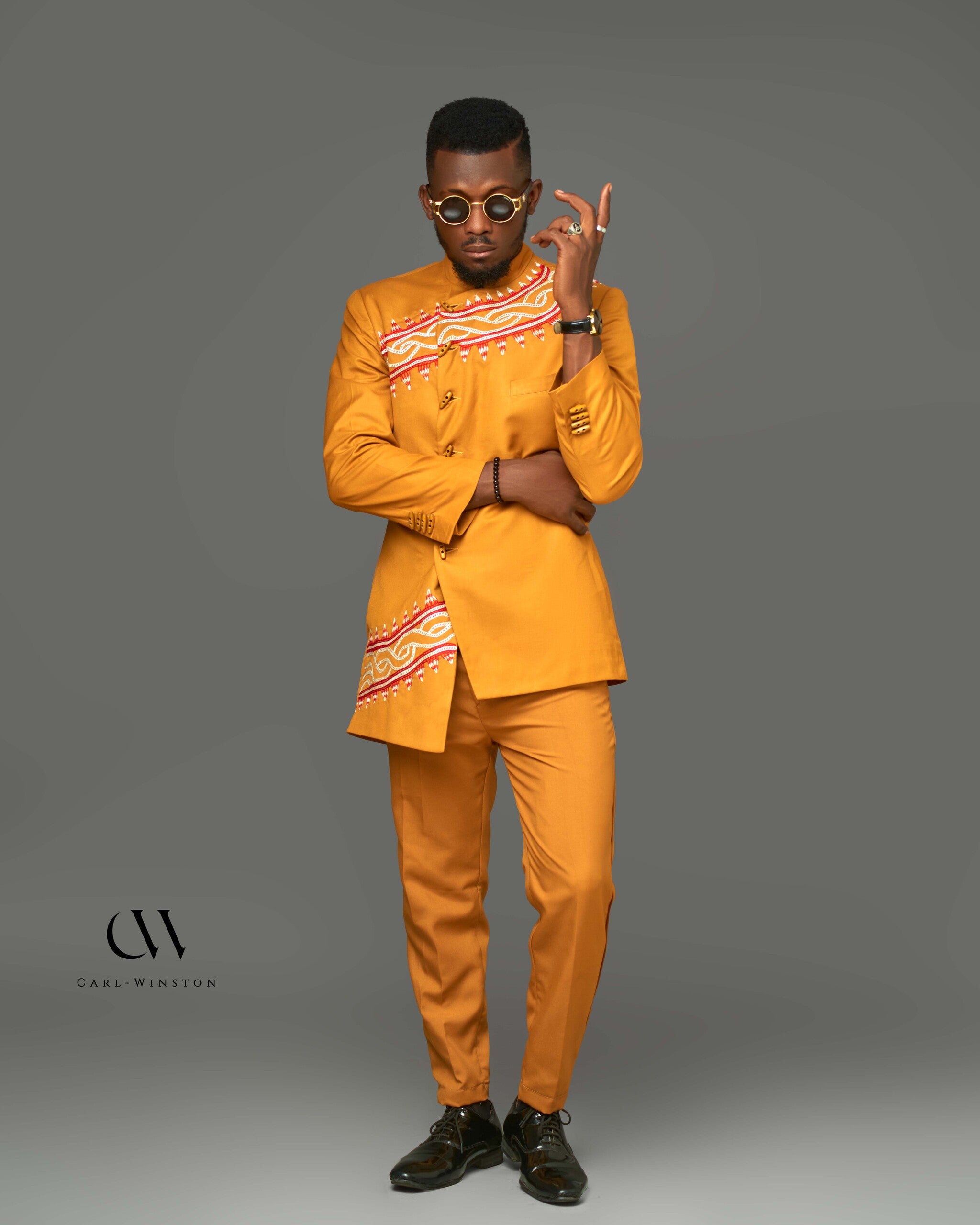 A striking gold Tikar Majesty Suit featuring intricate Toghu embroidery across the chest and blazer. Modeled with confidence, this two-piece set combines traditional Cameroonian artistry with modern tailoring, perfect for formal occasions and cultural events.