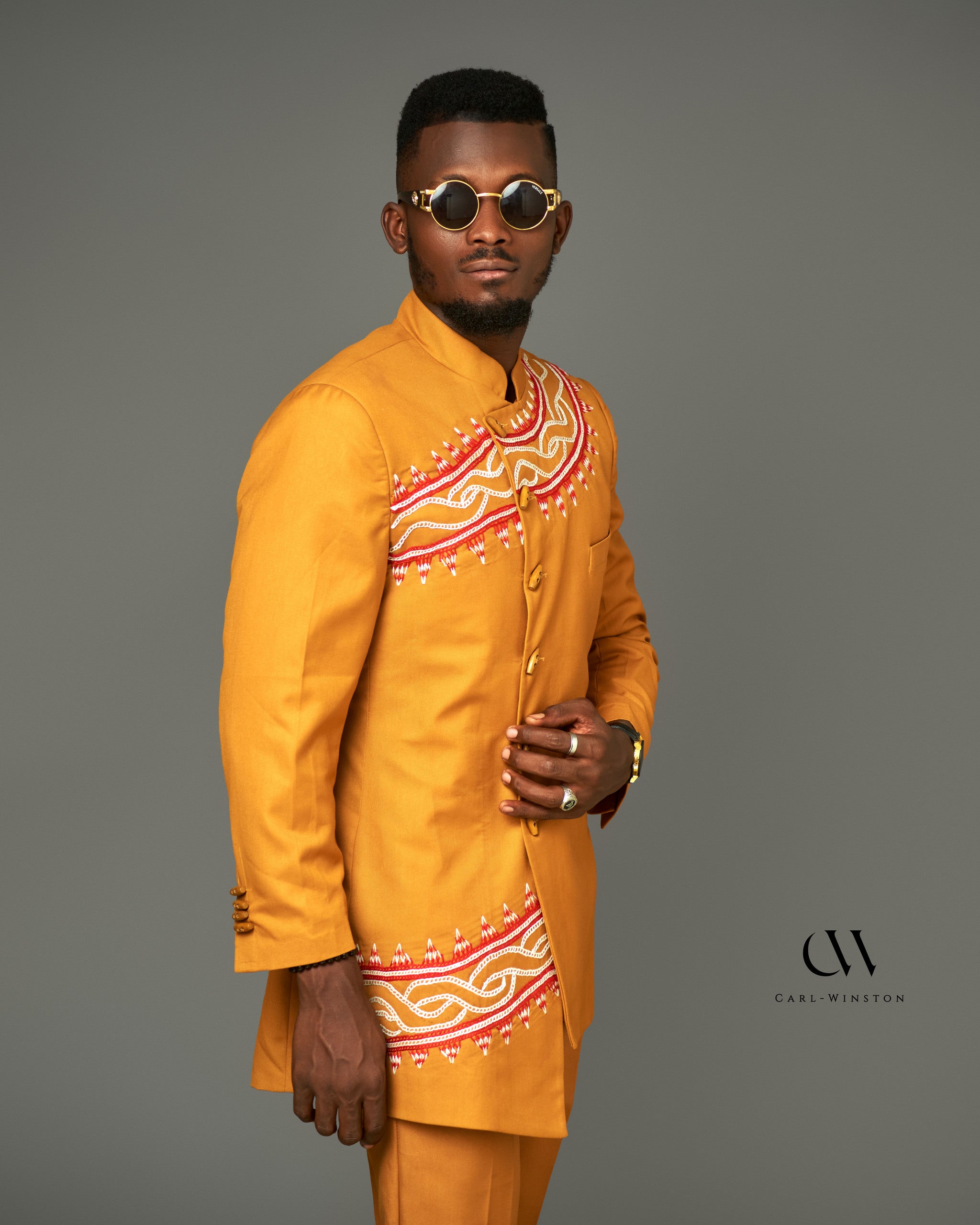A striking gold Tikar Majesty Suit featuring intricate Toghu embroidery across the chest and blazer. Modeled with confidence, this two-piece set combines traditional Cameroonian artistry with modern tailoring, perfect for formal occasions and cultural events.