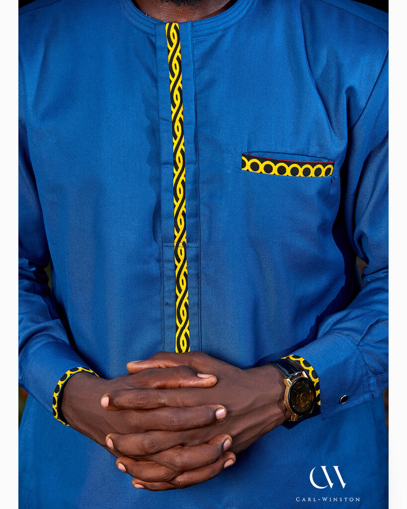 Close-up and full-body views of a male model wearing a tailored blue Elegant Atoghu Kaftan with yellow geometric embroidery, styled with matching pants and traditional hat, photographed outdoors among vibrant greenery and floral backdrops.