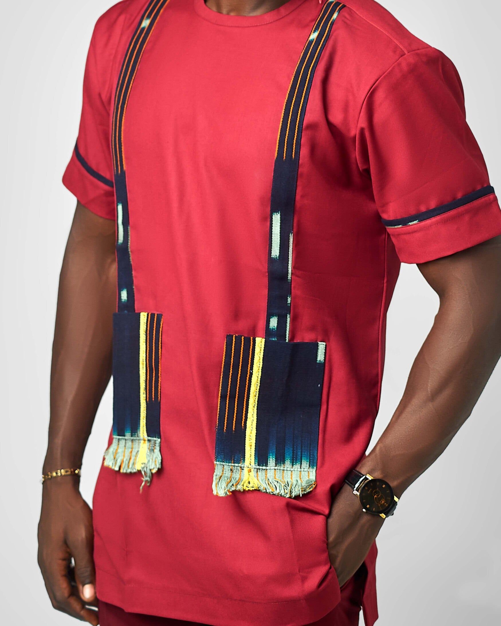A rich red short-sleeve tunic featuring bold woven fabric pockets with fringed edges, inspired by African textile heritage. Designed by Carl-Winston, this statement piece merges tradition with contemporary style.