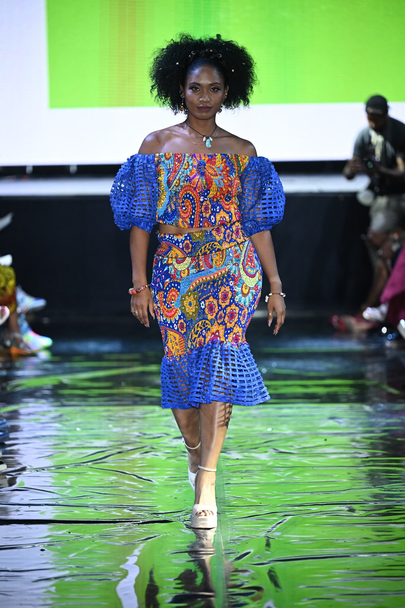 Model wearing a colorful dress on a runway with a green and black background