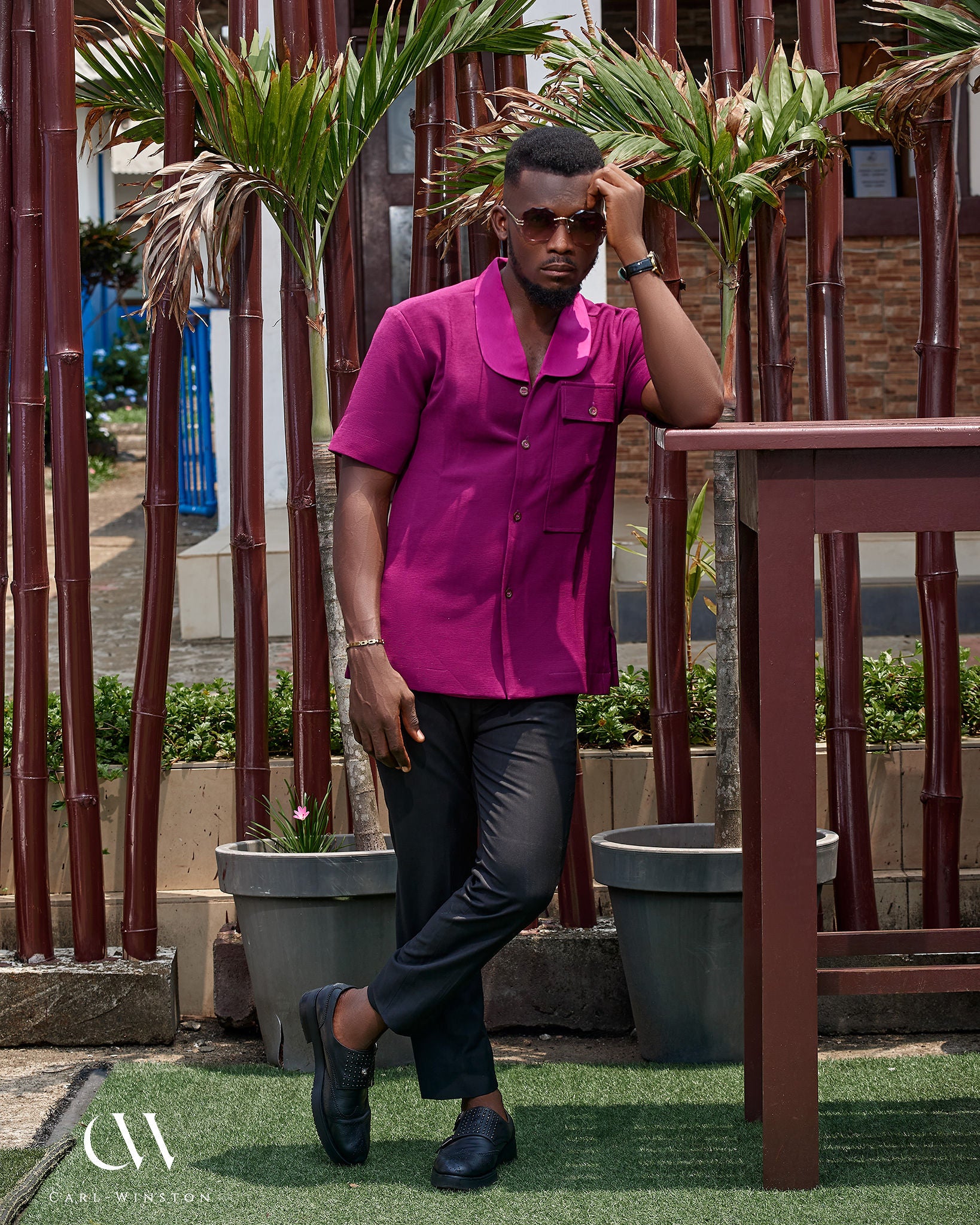 Man wearing Bamako Breeze Shirt in rich wine tone, standing confidently by bamboo stalks.