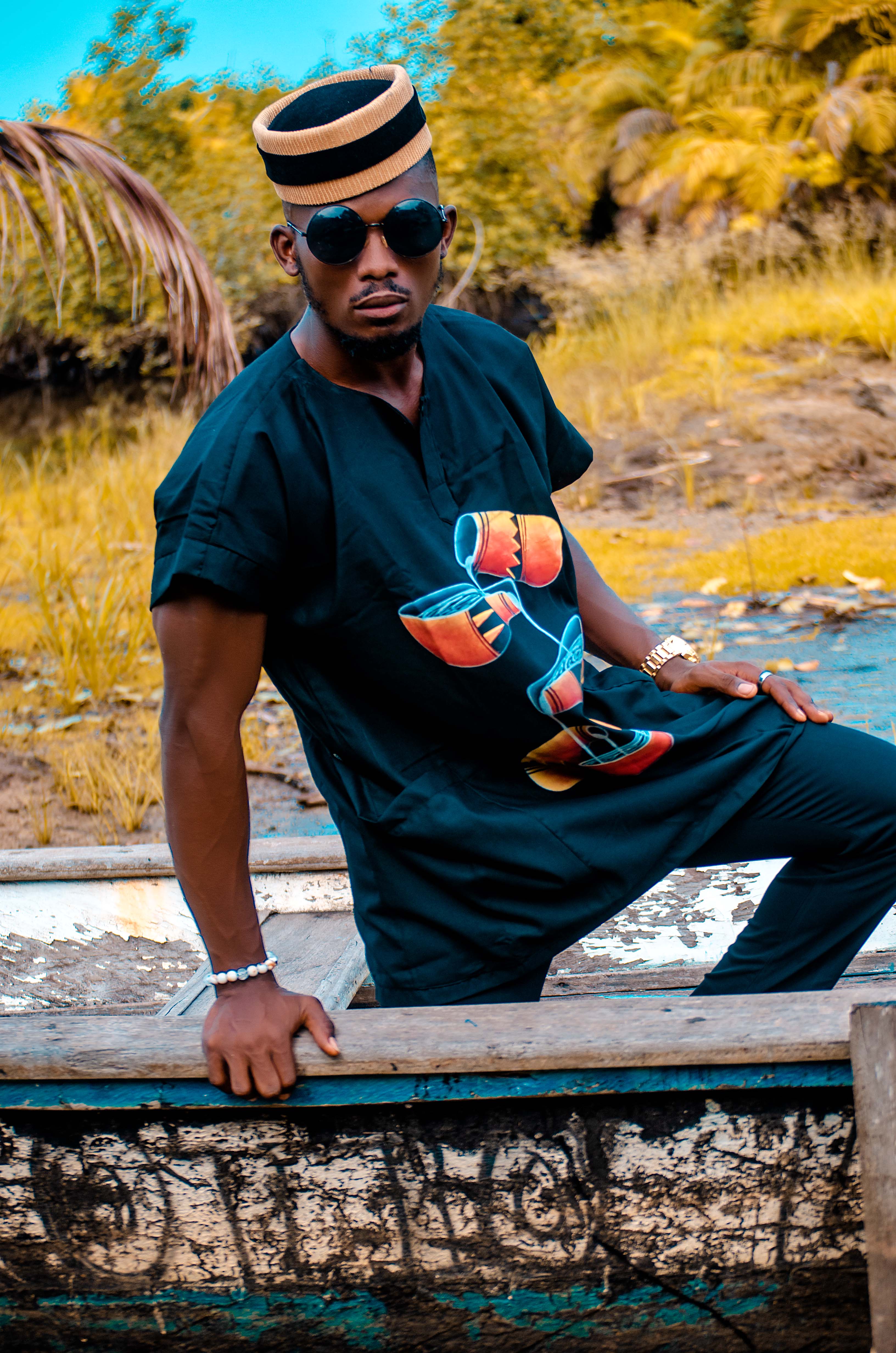  Carl-Winston black short-sleeve African tunic with a bold colorful drum graphic print paired with a traditional Cameroonian cap fusion of African heritage and contemporary fashion